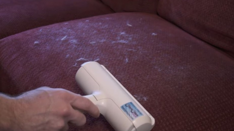 person using ChomChom Roller on red couch with pet fur