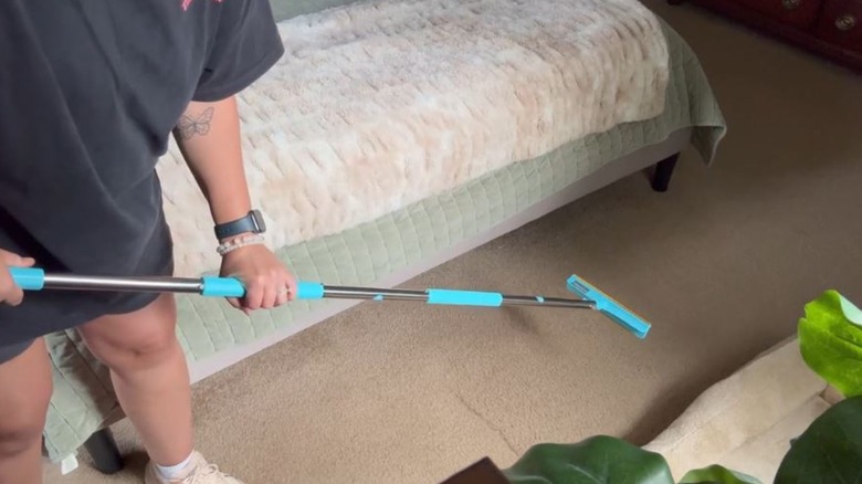 person using Uproot Cleaner Xtra rake on carpet with visible fur