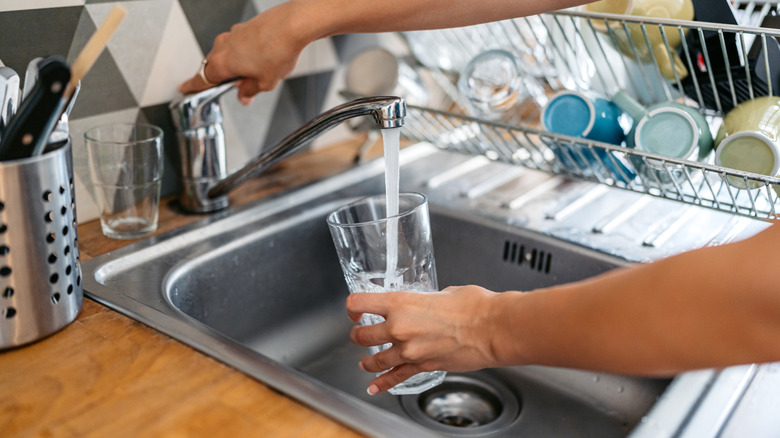 A person fills a glass with water from the kitchen faucet.