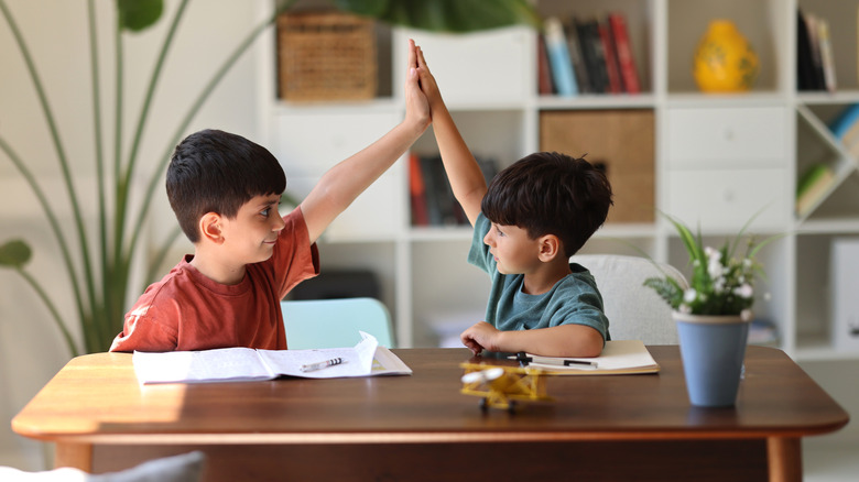 Two boys studying together at a single desk, high fiving