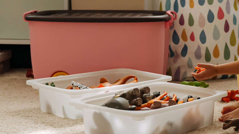 Child's hand taking toy out of plastic bin, with large bin in background