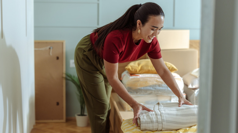 Woman placing folded blanket on top of bed.