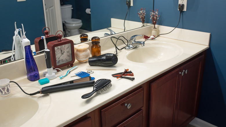 Disorganized bathroom counter with hair products, toothbrush, and clock