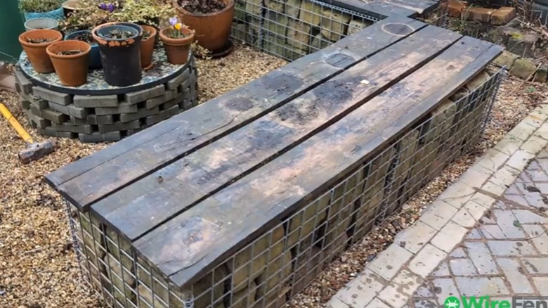 Completed gabion bench with wood plank seating surface on gravel