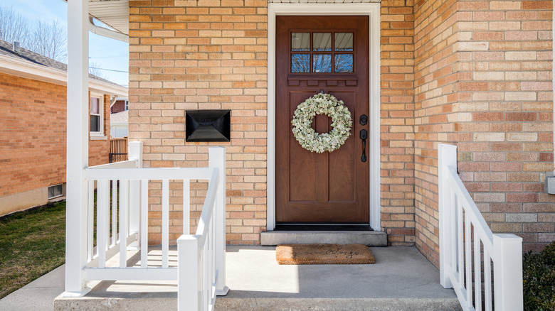 A small concrete front porch with brown door on house