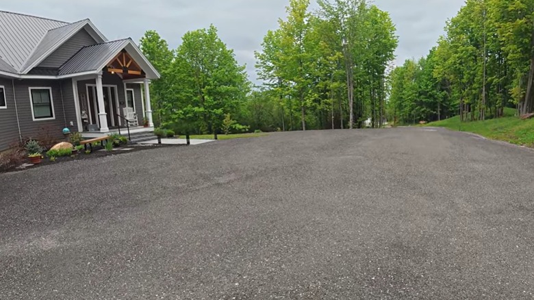 A gray house surrounded by trees and a large recycled asphalt driveway
