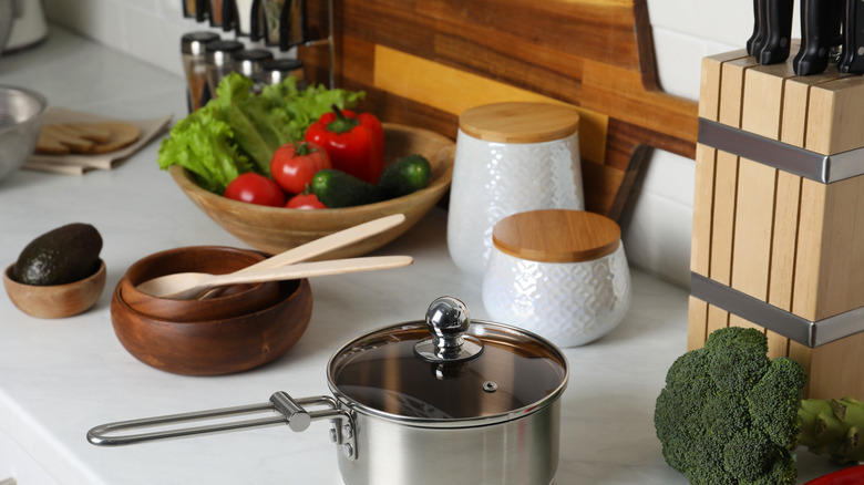 Kitchen counter cluttered with cooking supplies including a knife block and spice rack