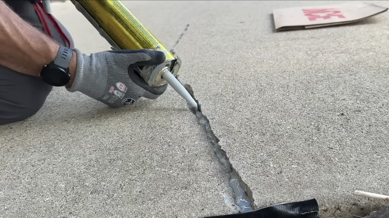 Man fills driveway cracks with concrete caulk.