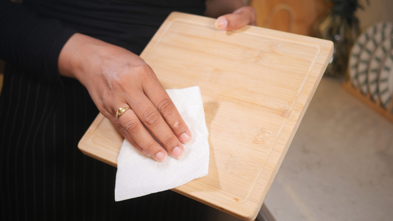 Close up of woman wiping down a wooden cutting board