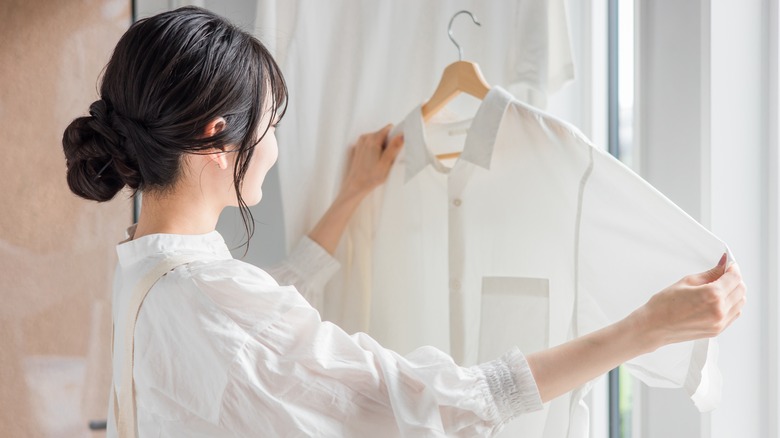 A woman holds up a stain-free shirt on a hanger to admire.