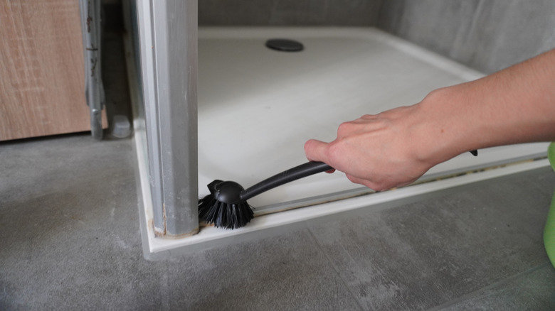 A person scrubs a dirty shower door track with a brush