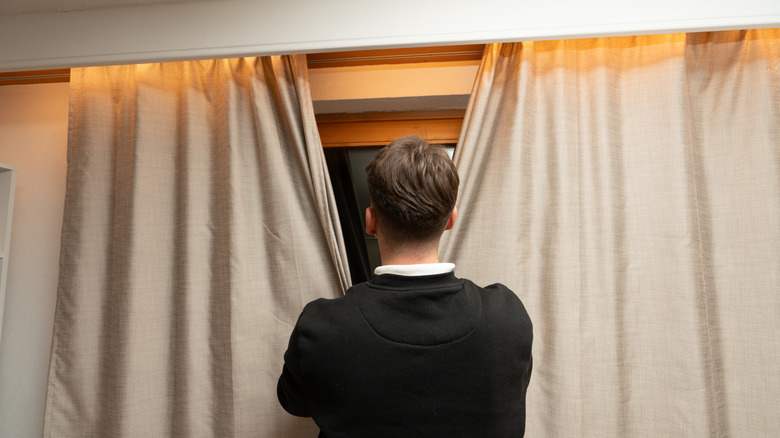 A man closing curtains