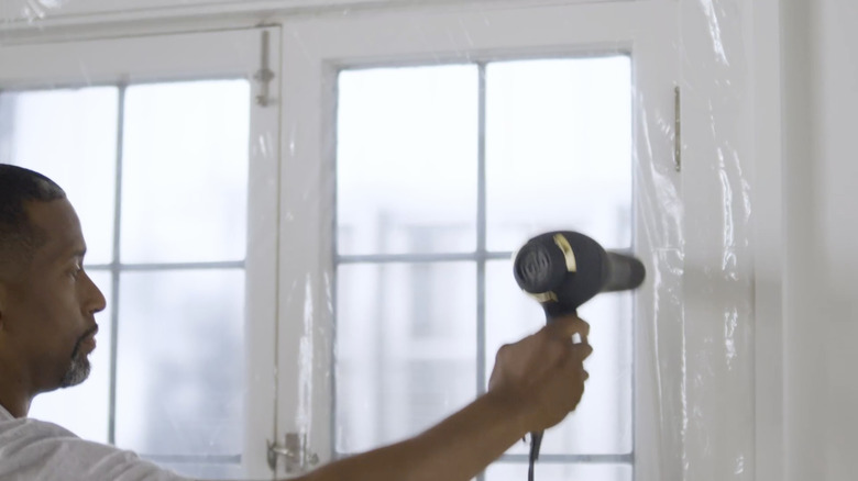 A man applying Duck's max-strength window film kit with a hairdryer