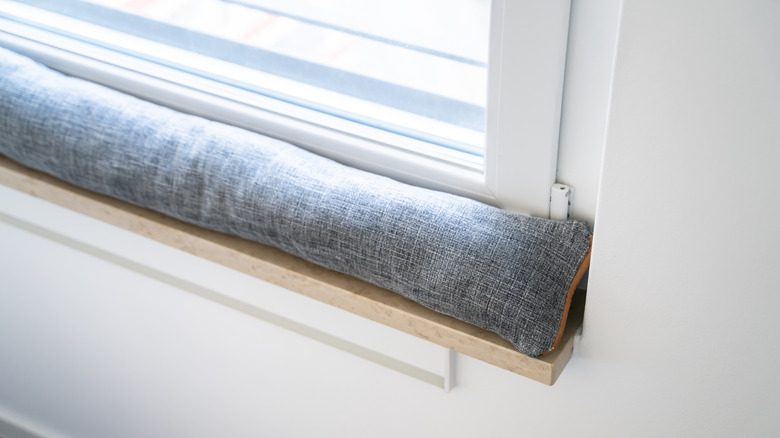 A fabric-covered draft excluder at the base of a window
