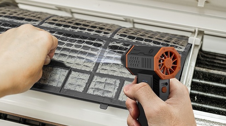 Hand using a cordless compressed air device to clean dirty AC filter