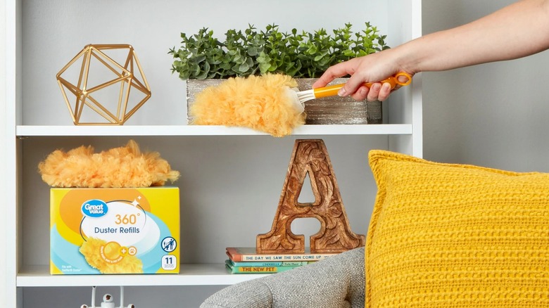 Someone's hand using a small duster to clean a white open shelf