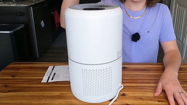 Man sitting in front of a white air purifier placed on a wood table