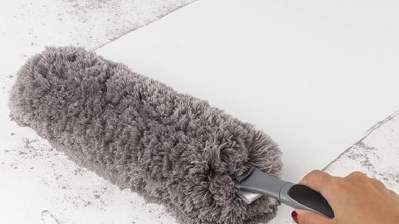 Hand using a gray duster to clean a white surface