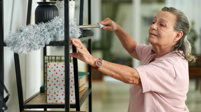 Woman using a duster to clean open shelves in her home