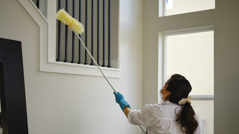 A woman using an extendable duster to clean staircase railings