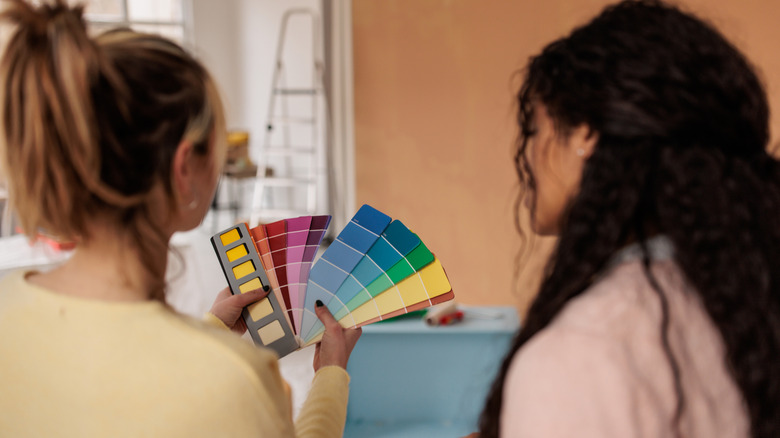 Two women considering paint color swatches in an orange room