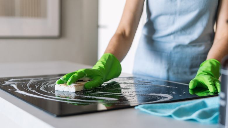 Person cleaning dirty electric stove top with gloves and a sponge
