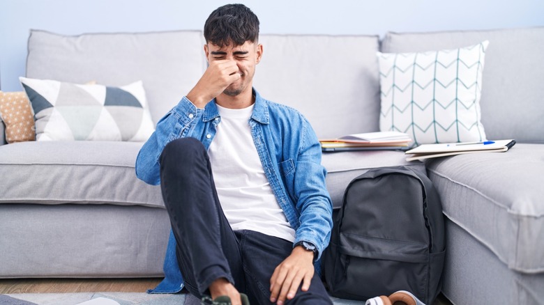 Man holding nose due to bad smell while coming from living room rug in front of couch