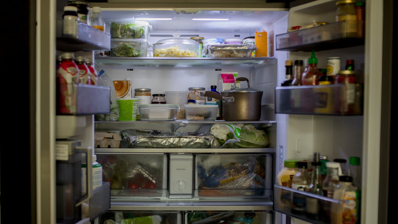 An open fridge filled with leftovers, condiments, drinks, and groceries