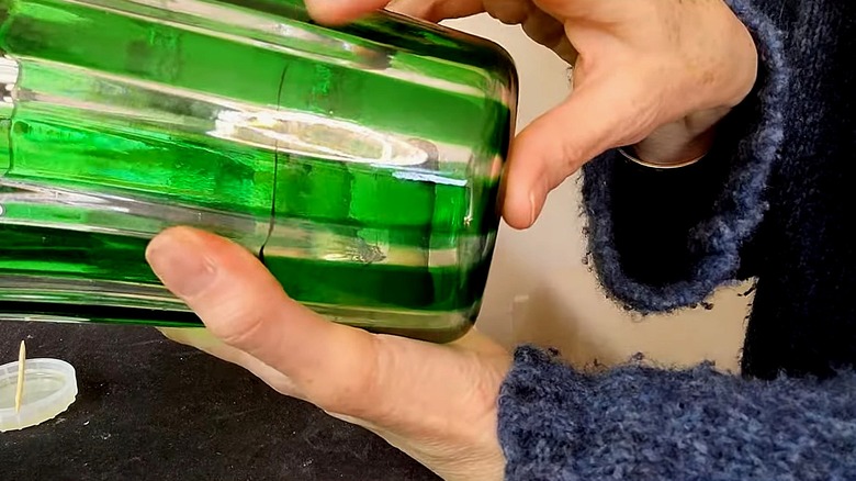 Person holds a clear and green glass vessel with a crack in the middle.