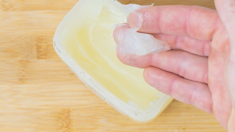 Hand scooping petroleum jelly from a container.