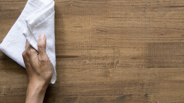 A hand cleaning a wood surface with a white cloth.