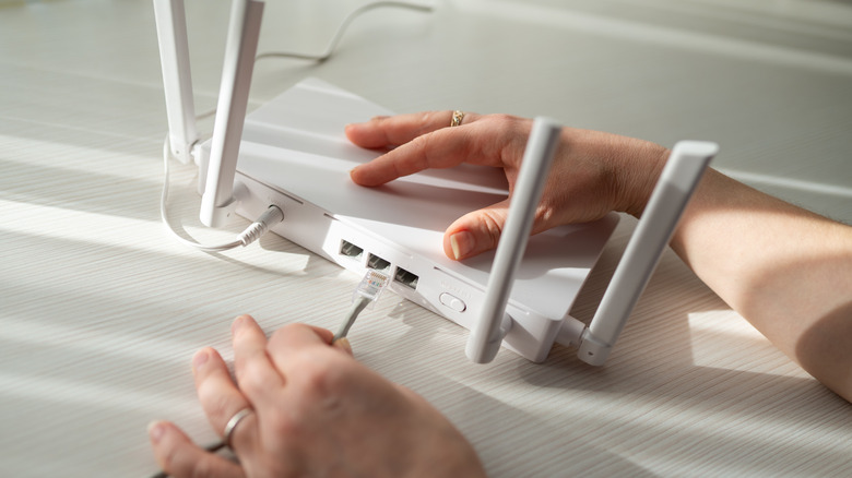 A pair of hands plugging in a Wi-Fi router resting on an empty desk