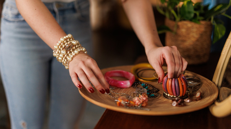 A person touching jewelry in a wooden tray