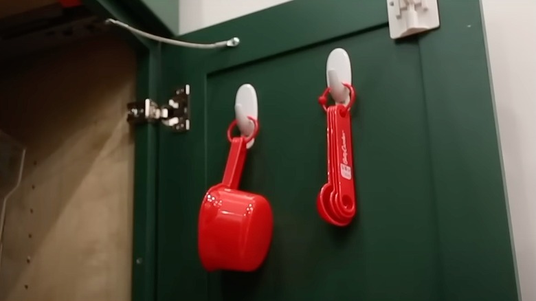 measuring cups and spoons hanging on plastic hooks inside a kitchen cabinet
