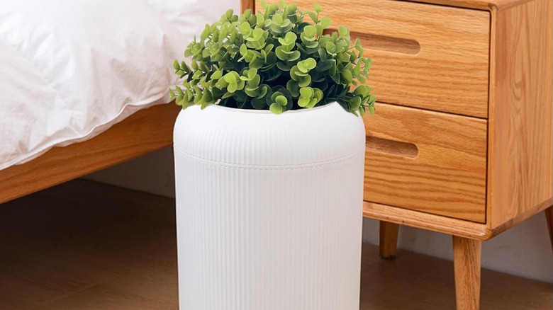 White trash can with artificial plants on top sitting in a bedroom