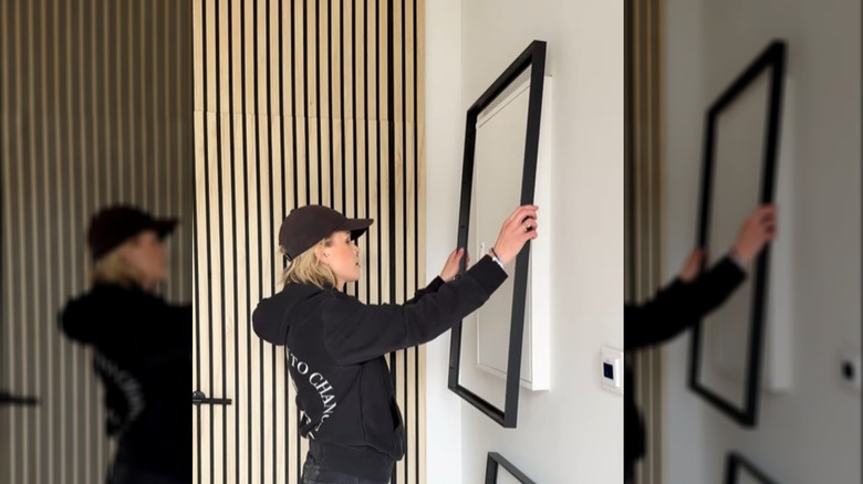 A person hangs an IKEA picture frame over a utility box on the wall.