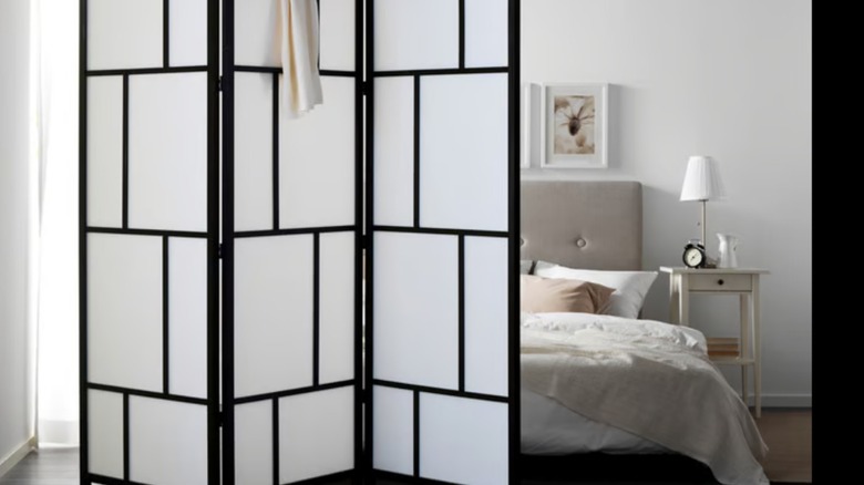 An IKEA RISOR room divider hides the bed from view of a combination laundry room and bathroom in a small home.