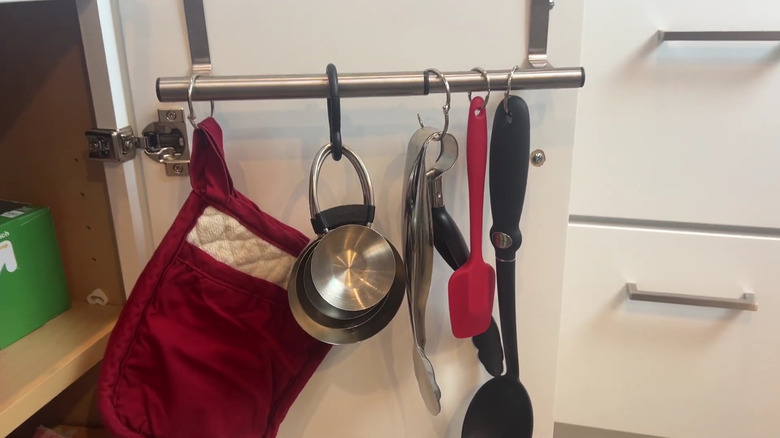 Oven mitts, utensils, and measuring cups hanging from a Dollar Tree towel bar