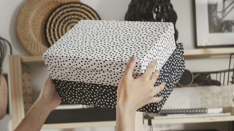 Two RÄTTAREN storage boxes with lids in someone's hands in the air