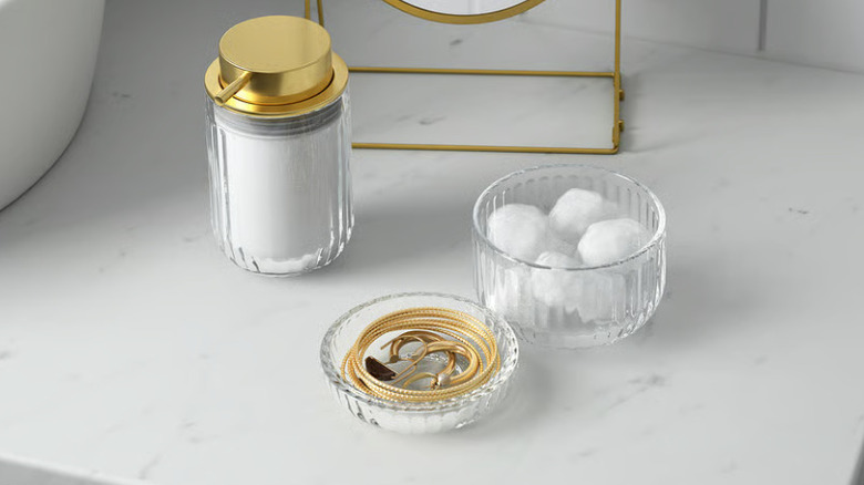 The SILVTJÄRN container with cotton swabs on one side and gold jewelry on the other on a bathroom counter