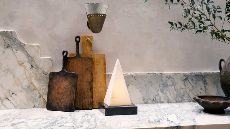 Veiny marble kitchen countertop and backsplash with decorative wood chopping boards and pyramid sculpture.