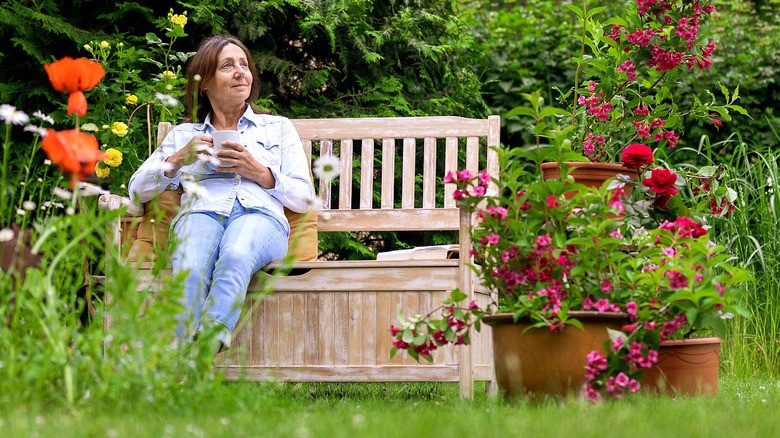 Person reading a book on a wooden bench in a garden surrounded by colorful flowers