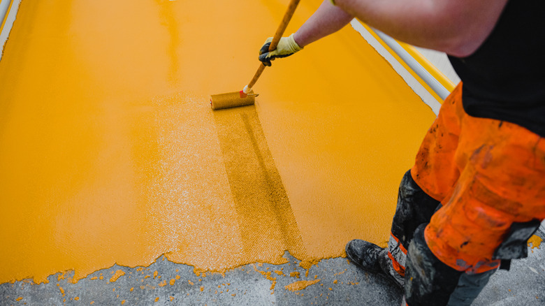 Someone with bright orange pants painting the floor a cheery yellow-orange over concrete
