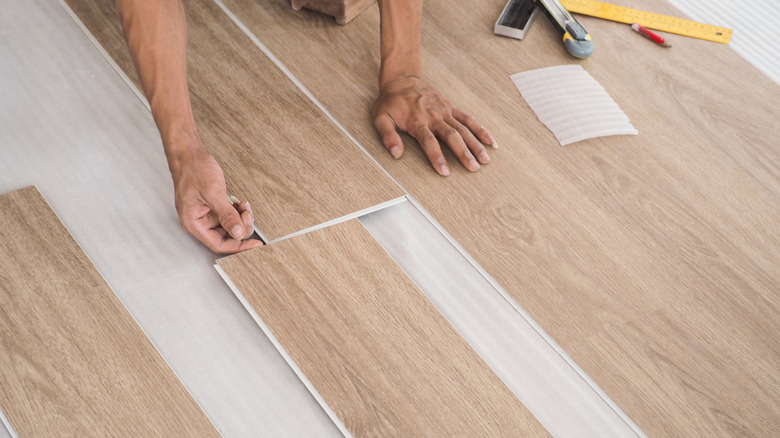 Someone installing vinyl flooring that looks like wooden planks