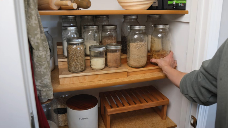 a person pulling a jar from a pantry with riser shelves