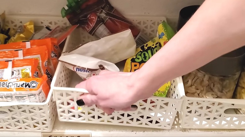 Hand lifting plastic basket containing bags of candy