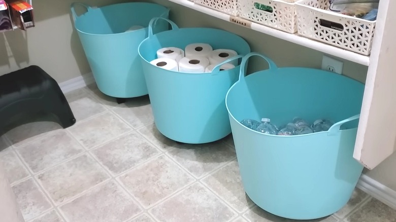 Large plastic tubs on rollers in the bottom of a pantry, holding paper towels and water bottles