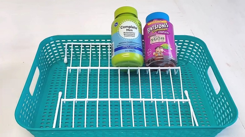 Dollar Tree tiered shelf with bent legs in a plastic bin holding vitamin bottles