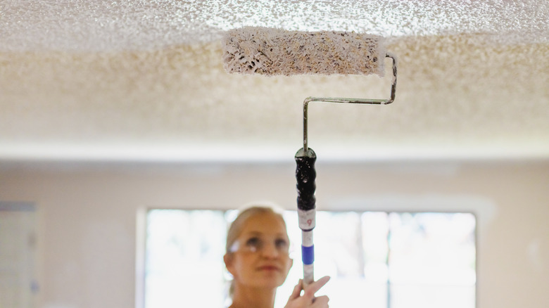 Close up of woman painting over textured ceiling with foam roller