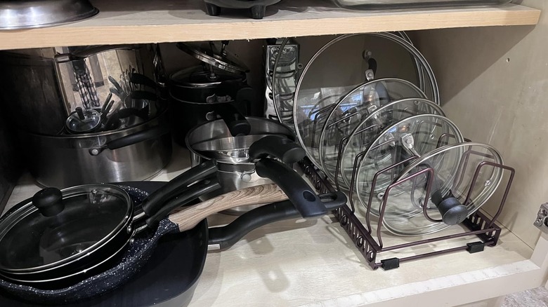 The inside of a cabinet showing pots and pans, along with lids arranged neatly in Toplife's Pot Lids Organizer Rack